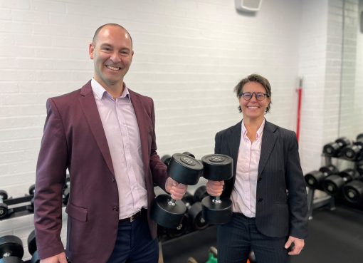 Two academics holding gym dumbells and posing for the camera smiling